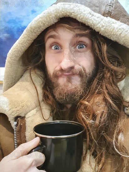 Portrait shot of a funny young man with a camping tin tea cup in his hand, looking at camera and