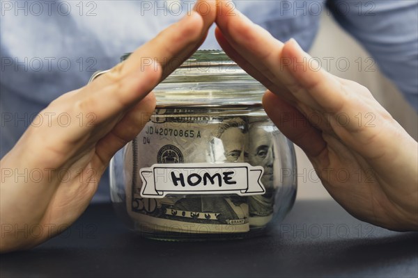 Unrecognizable woman holding Saving Money In Glass Jar filled with Dollars banknotes. HOME