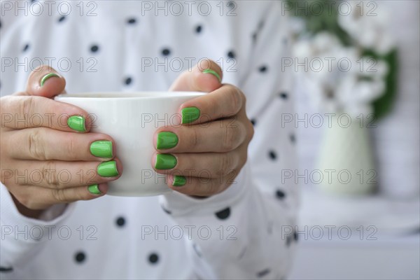 Manicured female hands with stylish green nails holding cup of coffee. Take a break for coffee