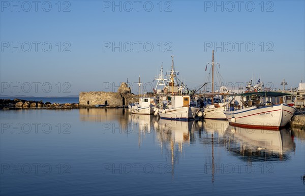 Fishing boats in the harbour and ruins of the Venetian castle, reflected in the sea, at sunset,