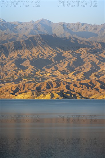 Blue Toktogul reservoir between dry mountain landscape, hilly mountains in the evening light,