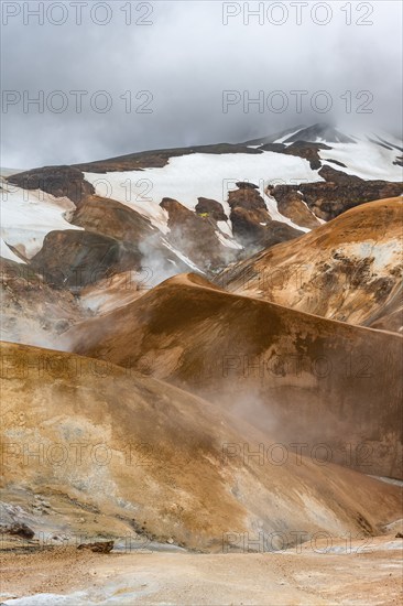 Hot springs and steaming stream between colourful rhyolite mountains with snowfields, Hveradalir