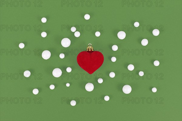 Red heart shaped Christmas tree bauble surrounded by snowballs on green background