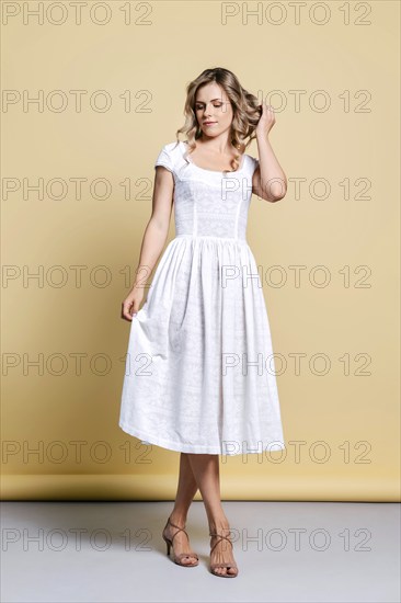 Beautiful joyful young woman in white sundress posing in studio