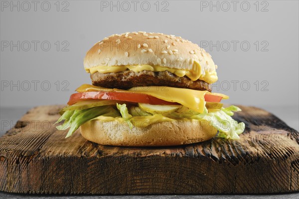 Beef cheeseburger with vegetables and cheesy sauce on wooden board, front view