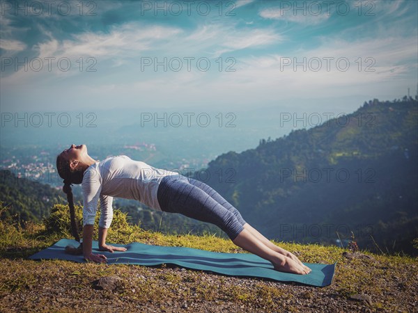 Woman doing Hatha yoga asana Purvottanasana plank pose outdoors in mountains. Vintage retro effect