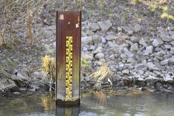 Yellow metric flood level marker in river with low water level