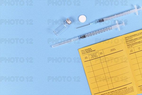 Vaccine concept with syringe, vial and yellow international certificate of vaccination on blue