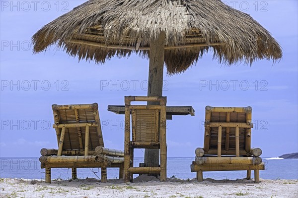Relaxing bamboo deck chairs with parasol on white sandy beach looking towards ocean at Pantai