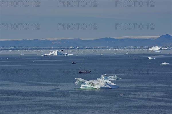Sailboat in a bay covered with icebergs, Disko Island in the background, Ilulissat, Arctic, Disko