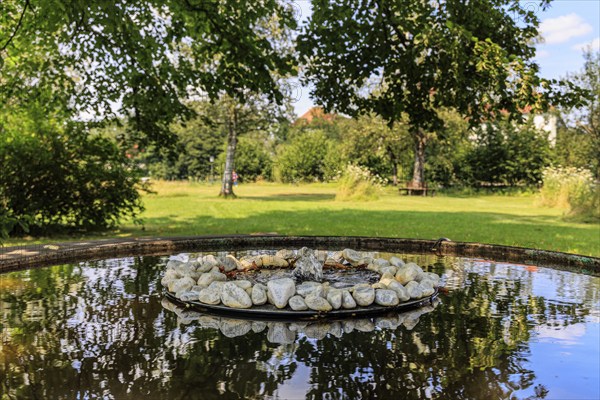Small fountain and water bowl with stones under trees, Schlehdorf Monastery, Bavaria, Germany,