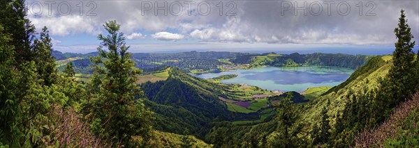 Wide panorama of the crater lake Lagoa Azul surrounded by lush green hills and clouds in the sky,