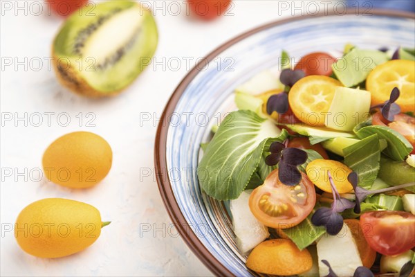 Vegetarian salad of pac choi cabbage, kiwi, tomatoes, kumquat, microgreen sprouts on a white