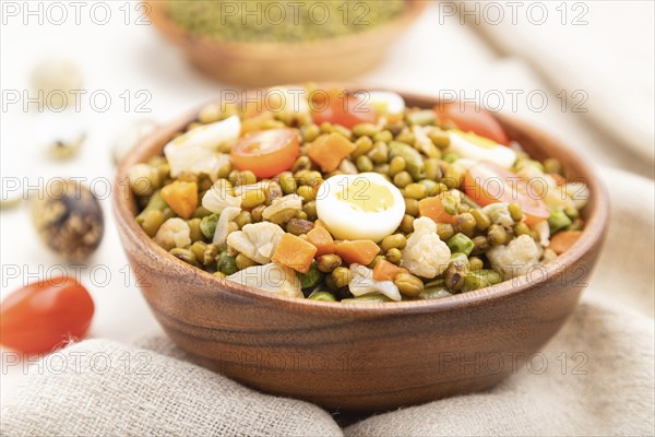 Mung bean porridge with quail eggs, tomatoes and microgreen sprouts on a white wooden background