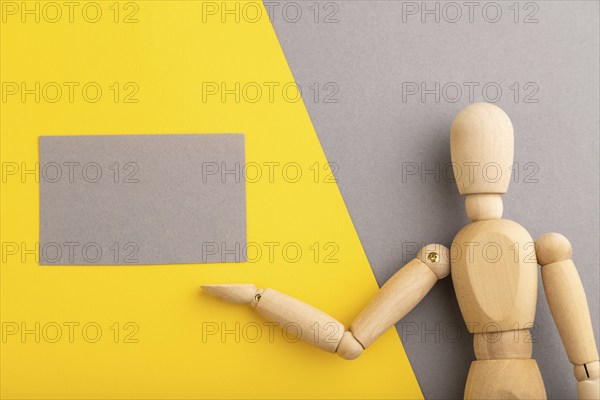Wooden mannequin holding gray blank poster on gray and yellow pastel background. copy space,