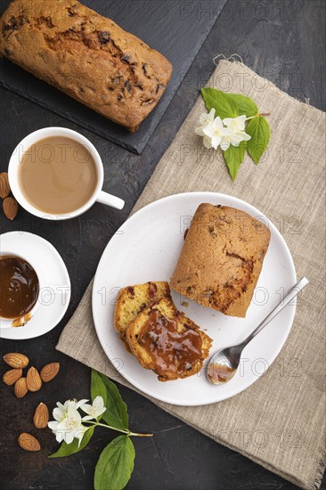 Homemade cake with raisins, almonds, soft caramel and a cup of coffee on a black concrete