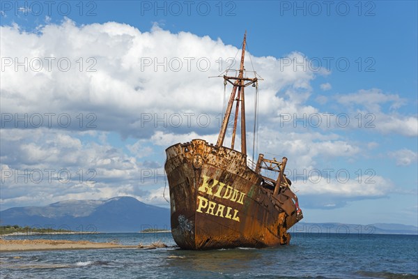 A rusty shipwreck protrudes from the water against a picturesque coastal backdrop, Dimitrios