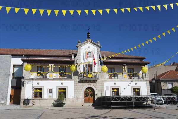 Historic building on a sunny square with yellow flags and festive decorations under a blue sky,