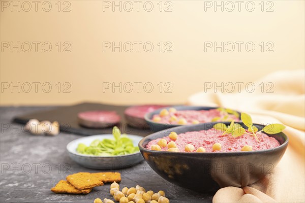 Hummus with beet and microgreen basil sprouts in ceramic bowl on a black concrete background and