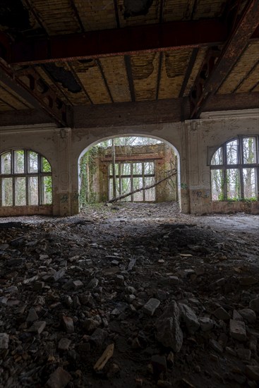 Interior view of a dilapidated building with arched windows and debris on the floor,
