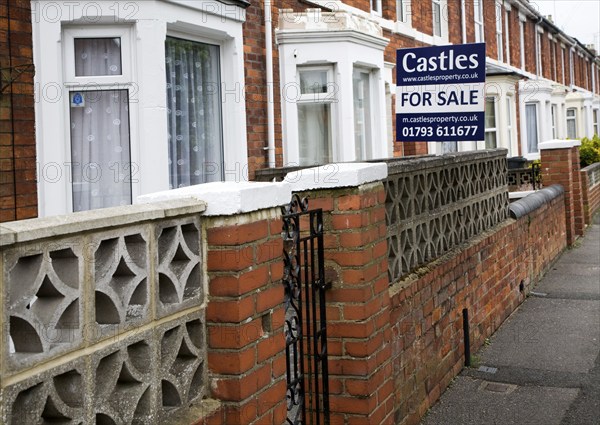 Estate agent for sale sign outside red brick terraced house in central Swindon, England, United
