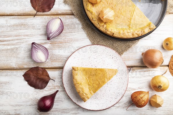 Autumn onion pie decorated with leaves and cup of coffee on white wooden background and linen