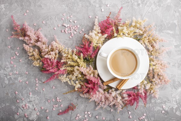 Pink and red astilbe flowers and a cup of coffee on a gray concrete background. Morninig, spring,