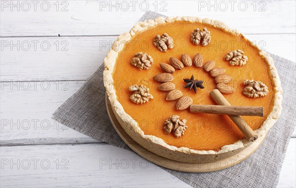 Traditional american sweet pumpkin pie decorated with nuts, on white wooden background. close up