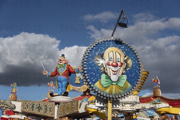 Colourfully decorated carousel with clown figure and blue sky in the background at a fairground,