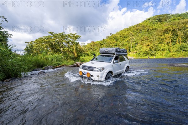 Toyota off-road vehicle with roof tent drives through a wide river in the rainforest, Alajuela