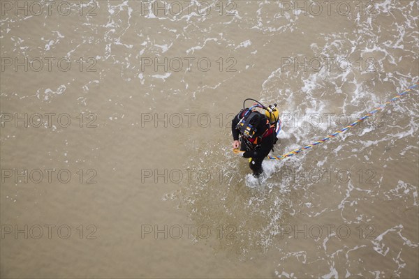Looking down from above at professional diver on a beach about to enter the sea to work on the pier