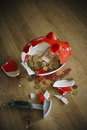 Symbolic photo on the subject of saving. An open, broken piggy bank with coins and banknotes stands