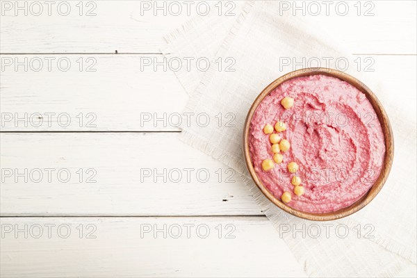 Hummus with beet in wooden bowl on a white wooden background and linen textile. Top view, flat lay,