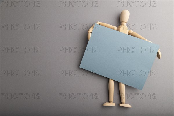 Wooden mannequin holding blue blank poster on gray pastel background. copy space, isolated,