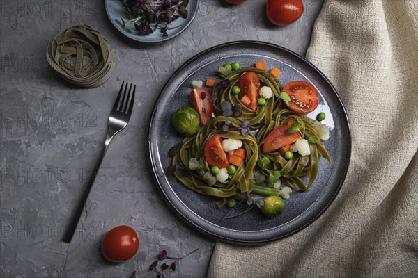 Tagliatelle green spinach pasta with tomato, pea and microgreen sprouts on a gray concrete