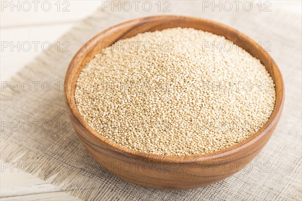 Wooden bowl with raw white quinoa seeds on a white wooden background and linen textile. Side view,