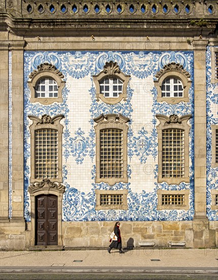 Woman passes by the facade of Igreja do Carmo church, adorned with intricate blue and white tiles,