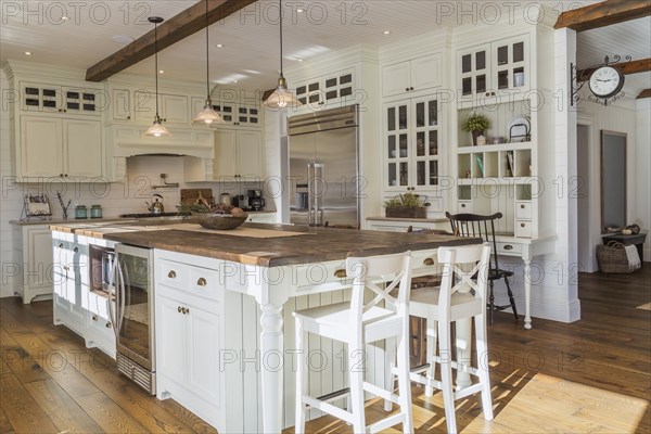 White painted maple wood antique style cabinets with tan coloured quartz countertops, island with