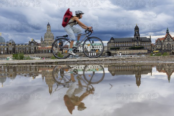 The Dresden silhouette with a cyclist and dark clouds behind the Church of Our Lady is reflected in