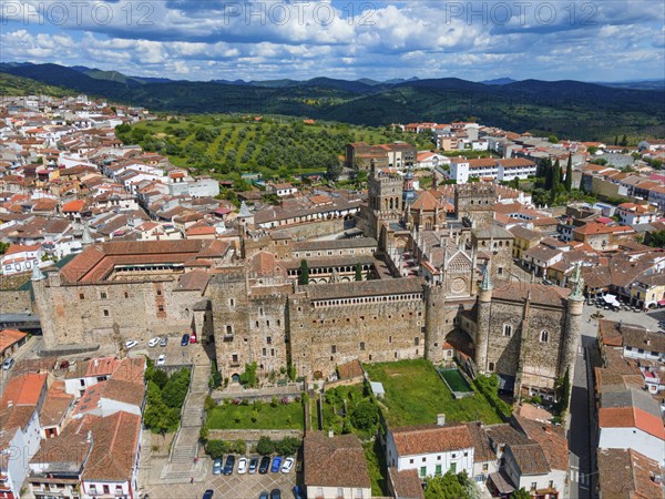 Aerial view of an old monastery with red roofs and surrounding green areas in a village in Spain.