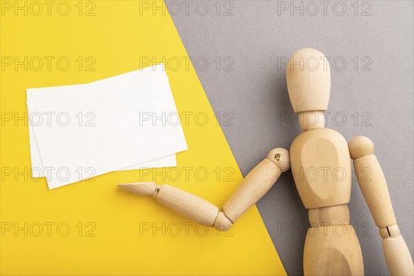 Wooden mannequin holding white blank poster on gray and yellow pastel background. copy space,