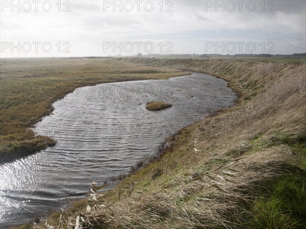 Marshland behind vegetated shingle with lagoon water bounded by costal defence sea wall, Alderton,