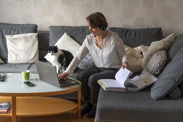Woman, mid-50s, works from home, with laptop and communicates with colleagues via headset, home