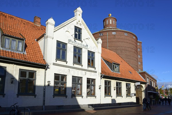 A white traditional building with a tiled roof in the foreground in front of an unusual round tower