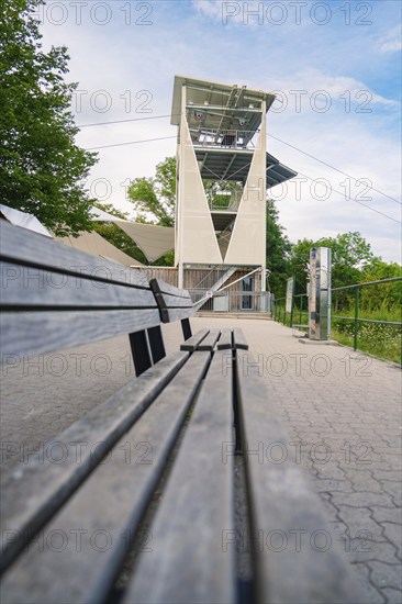 A long wooden bench runs along a hiking trail with a view of a modern observation tower,
