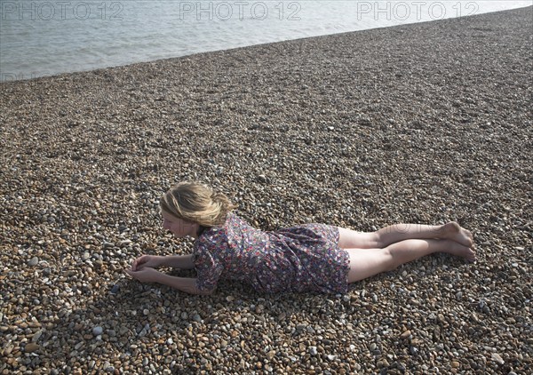 Model released young teenage girl wearing floral dress lies on shingle beach near the sea