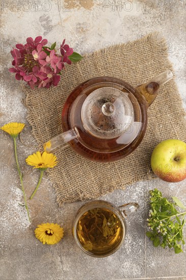 Red tea with herbs in glass teapot on brown concrete background and linen textile. Healthy drink