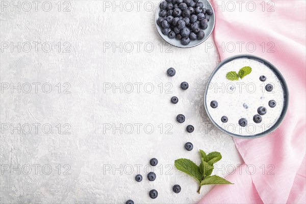 Yogurt with blueberry in ceramic bowl on gray concrete background and pink linen textile. top view,