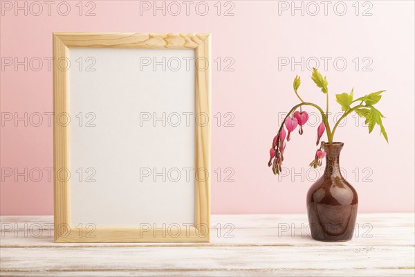Wooden frame with pink dicentra, broken heart in ceramic vase on pink pastel background. side view,