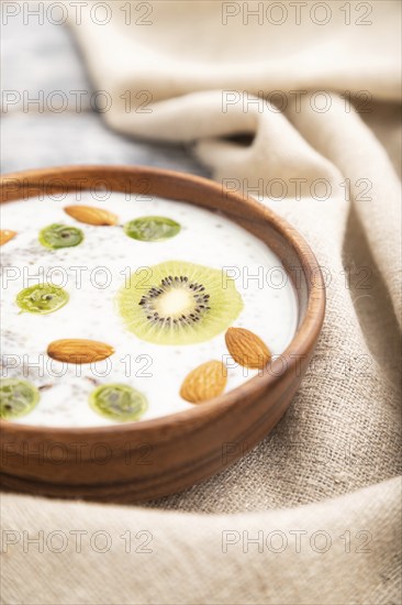 Yogurt with kiwi, gooseberry, chia and almonds in wooden bowl on gray wooden background and linen